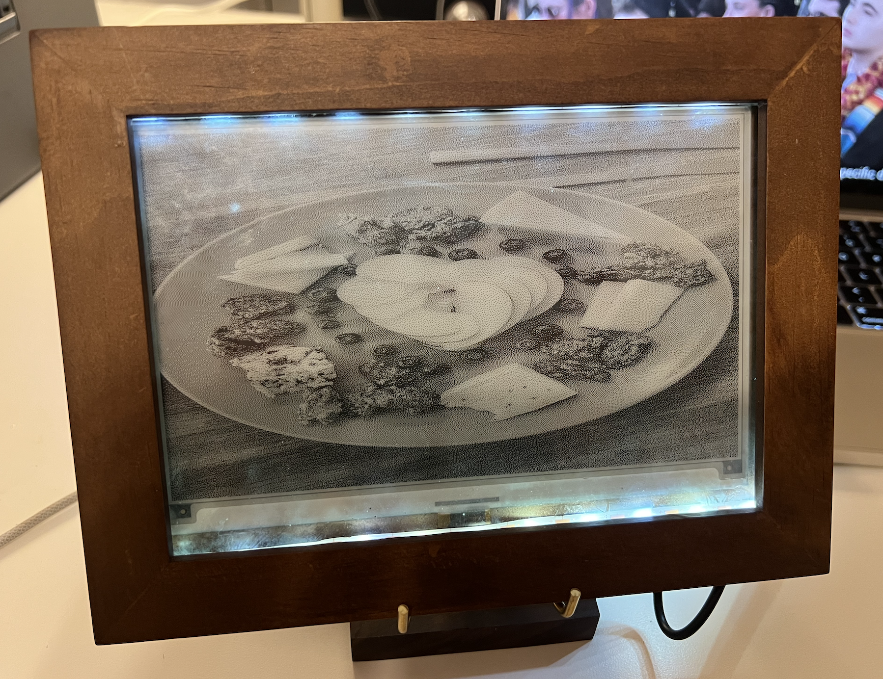 E-paper picture frame in a wooden frame showing a grayscale photo of a cheese board